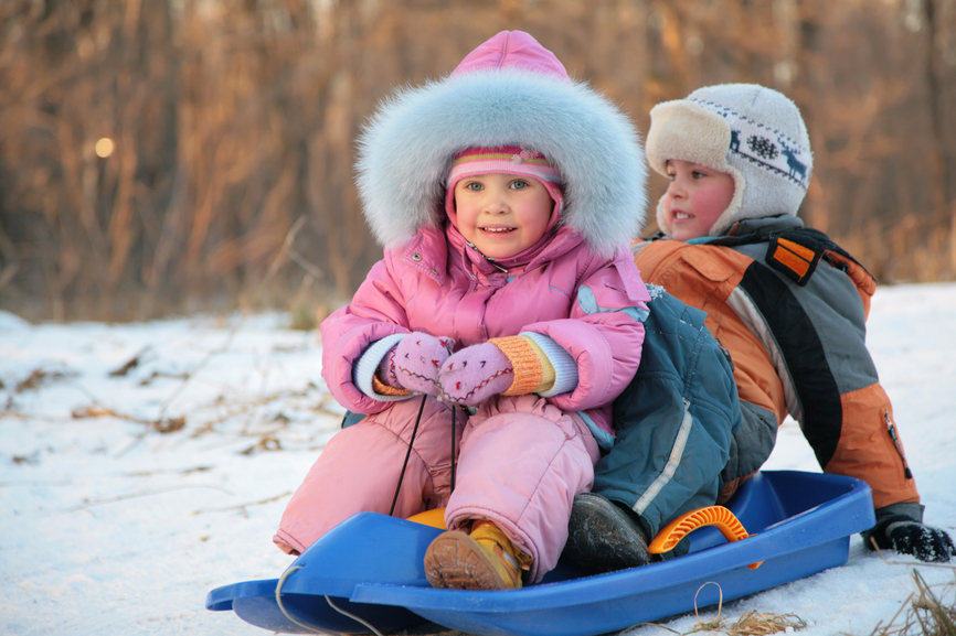 children  sits on plastic sled in park in winter