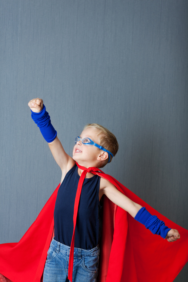 Little boy in super hero costume pretending to fly against blue wall