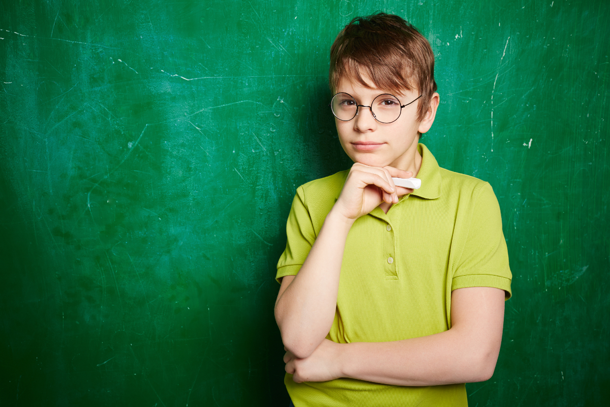 Portrait of cute schoolboy in eyeglasses looking at camera by the blackboard