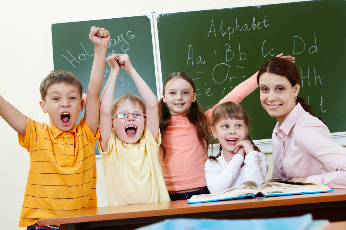 Portrait of joyful schoolchildren showing gladness with their teacher near by